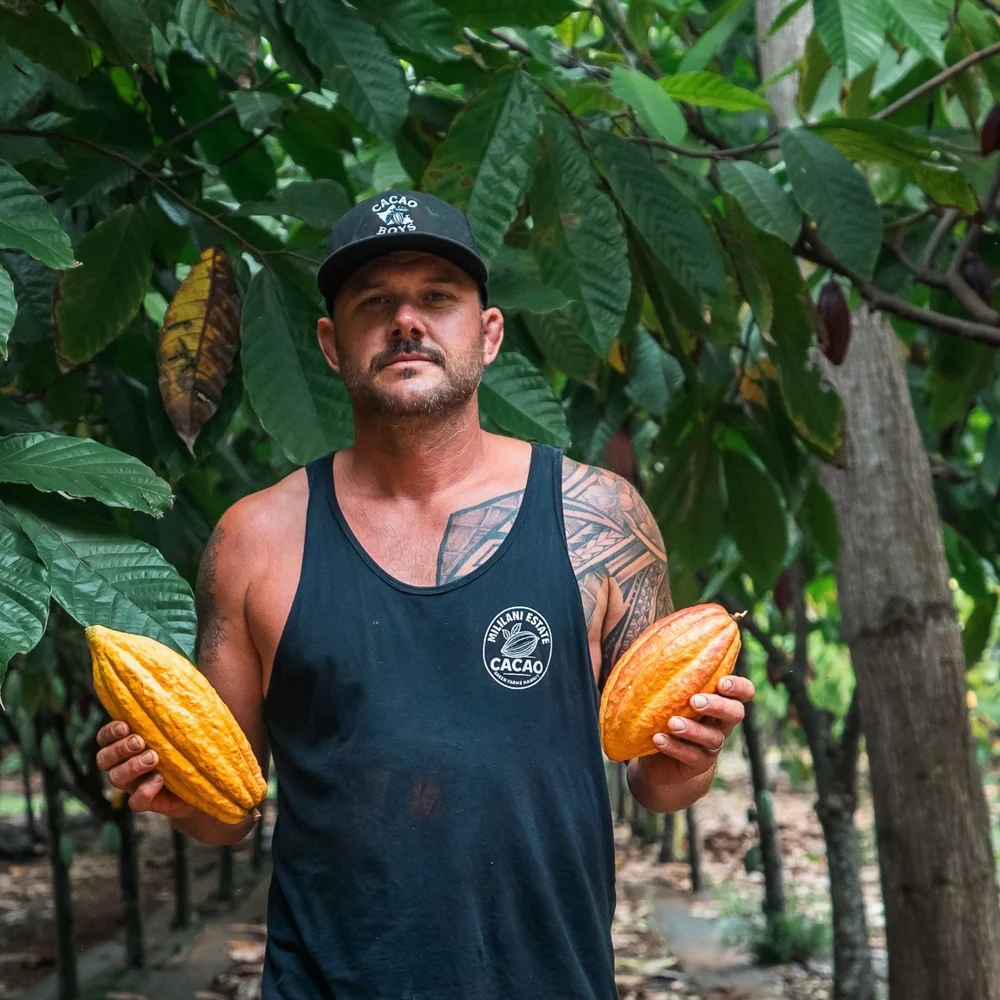 Pete in the orchard holding two ripe cacao pods
